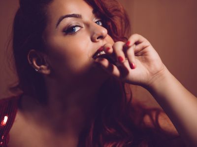Verführerische Frau mit roten Haaren, die auf ihren Finger beißt und einen intensiven Blick in die Kamera wirft