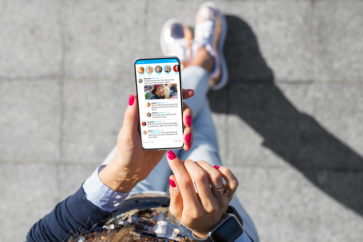 Eine Frau, die auf einem Bürgersteig sitzt und auf ihrem Smartphone eine Dating-App benutzt und benching befürchtet.