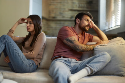 Ein nachdenkliches Paar sitzt mit Abstand auf einem Sofa, beide schauen in entgegengesetzte Richtungen – symbolisiert emotionale Distanz, Trennung oder den Wunsch nach einem Neuanfang.