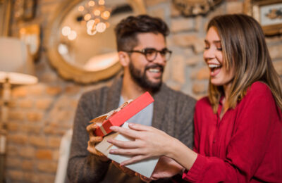 Junger Mann überreicht lachender Frau ein Geschenk – kleine Aufmerksamkeit beim ersten Treffen nach dem Dating-App-Match