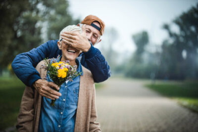 Älteres Paar im Park, Mann überrascht lachende Frau mit kleinem Blumenstrauß