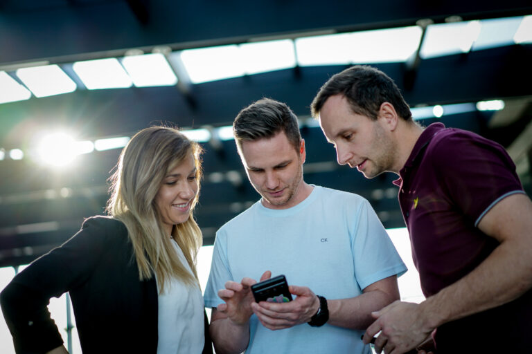 Drei junge Menschen schauen gemeinsam auf ein Smartphone mit der Diner Date Dating App