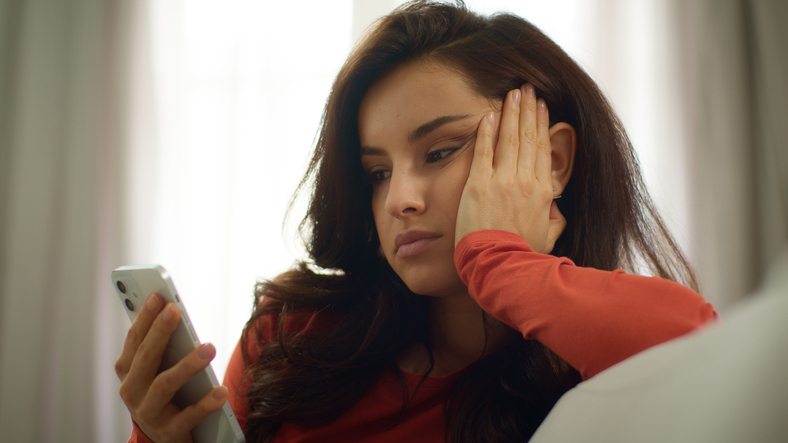 Eine junge Frau blickt erschöpft und frustriert auf ihr Smartphone, ein Symbol für die Dating-Müdigkeit, die viele Frauen zu einem bewussten Männer-Entzug bewegt.