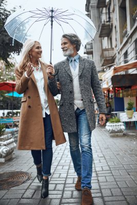 Reifes Paar lachend unter transparentem Regenschirm in der Stadt – symbolisiert unkompliziertes und diskretes Casual Dating.