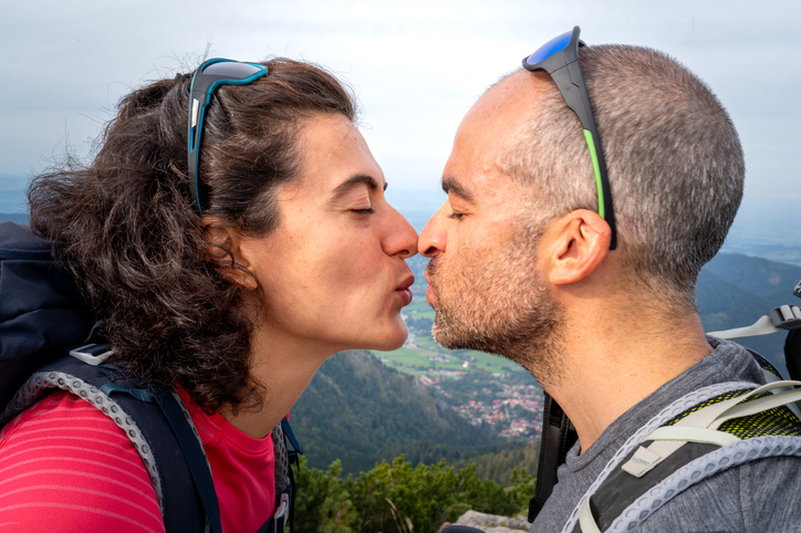 Pärchen küsst sich auf Berggipfel – Symbol für Liebe, Abenteuer und erfüllte Partnerschaft durch seriöses Online-Dating