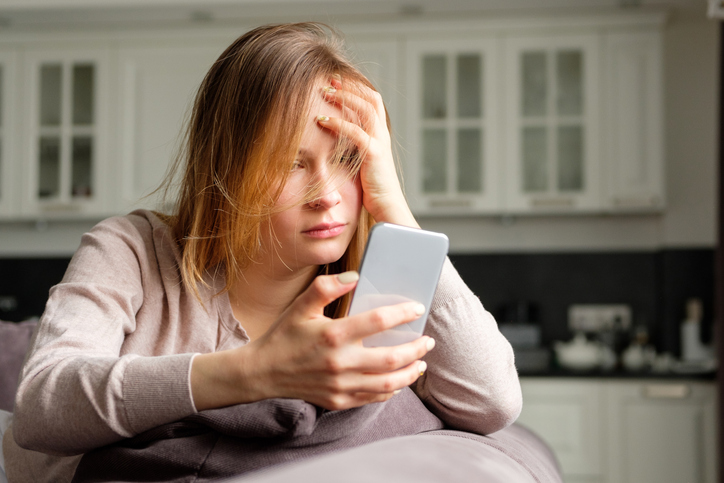Besorgte Frau blickt auf Smartphone nach Datenklau bei Dating-App.
