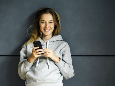 Lachende junge Frau hält Smartphone in der Hand – Diner Date App für authentisches Dating