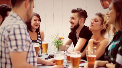 Vier Freunde lachen und trinken Bier auf einer Terrasse – Gruppendate ShakeDate App