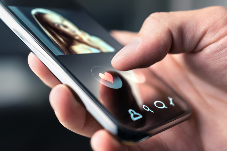Hand wischt auf Smartphone-Display mit Dating-App, Herzsymbol wird gedrückt - Lovoo Alternative