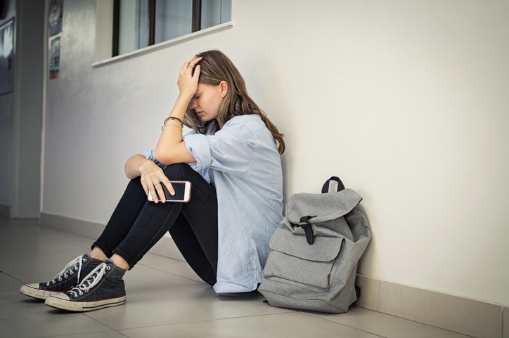 Junge Frau sitzt verzweifelt mit Smartphone auf dem Boden, symbolisiert Einsamkeit oder Frustration im digitalen Zeitalter.