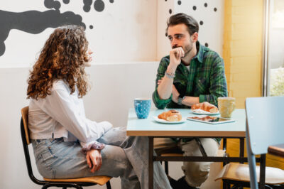 Junges Paar sitzt sich wortkarg gegenüber bei einem belanglosen Date im Café, sie schaut weg, er stützt den Kopf in die Hand.