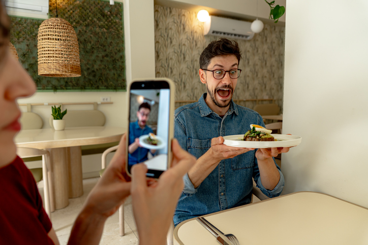 Mann posiert überschwänglich mit Teller im Restaurant, Date fotografiert ihn – Foodie Call / Gratis-Essen beim Date.