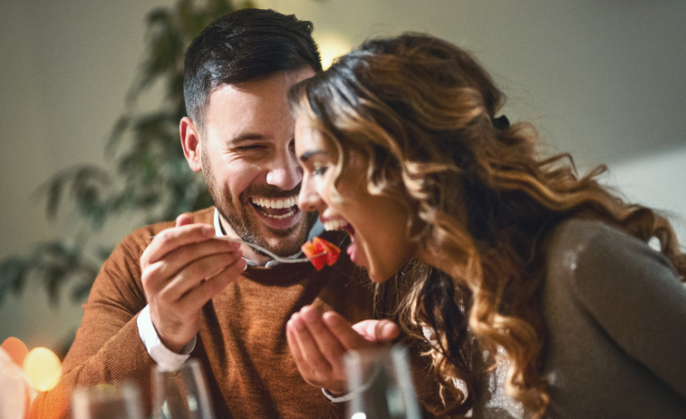 Paar beim Dinner, Mann füttert Frau mit einem Löffel – romantische Szene als Symbolbild für „Foodie Call“ (Gratis-Essen beim Date).