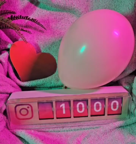 Rosa beleuchteter Counter mit Zahl 1.000, weißem Ballon und Herz – Diner Date feiert 1.000 Instagram-Follower (Meilenstein der Dating-App).