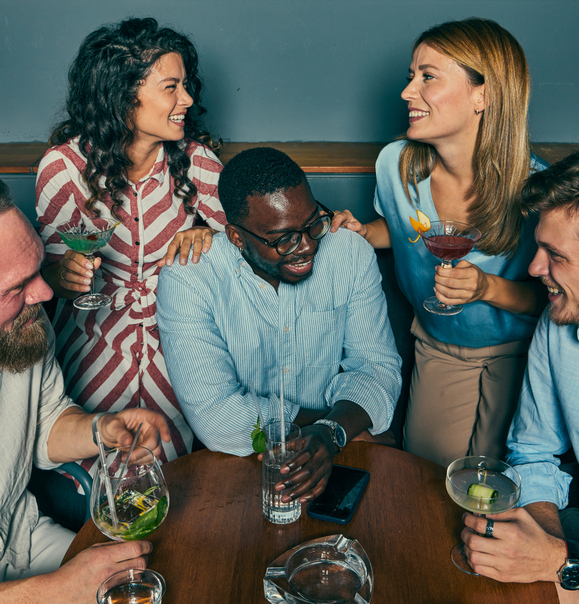 Freunde sitzen in einer Bar zusammen, lachen und trinken Cocktails – Friendfluence und Dating mit Freunden, Profilcheck und Gruppendates.