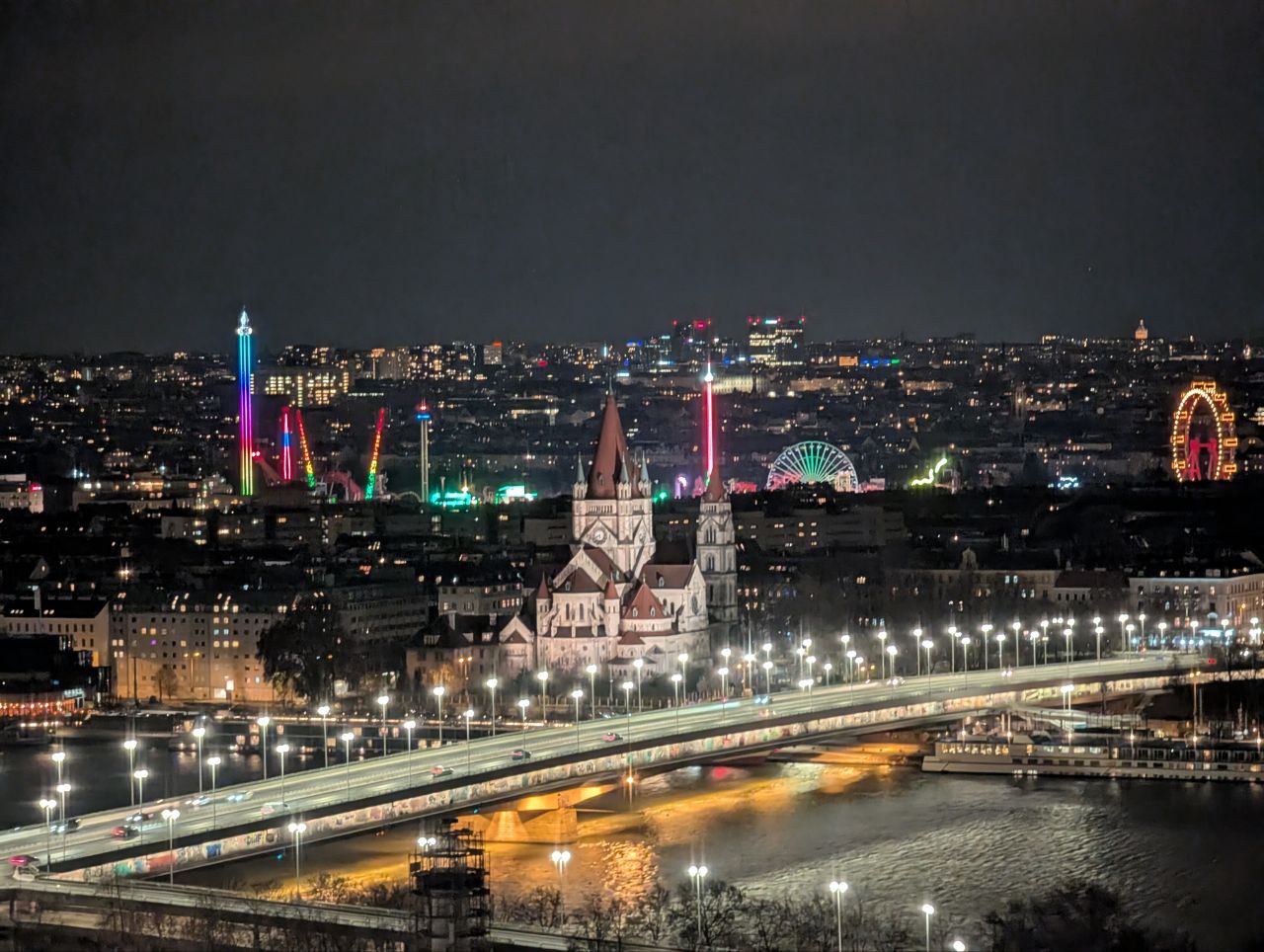 Nächtlicher Ausblick über Wien mit beleuchteter Reichsbrücke, der Kirche St. Franz von Assisi und dem bunt leuchtenden Prater – Abschluss unseres Start-up Trips zur GetaChef Launch Party.