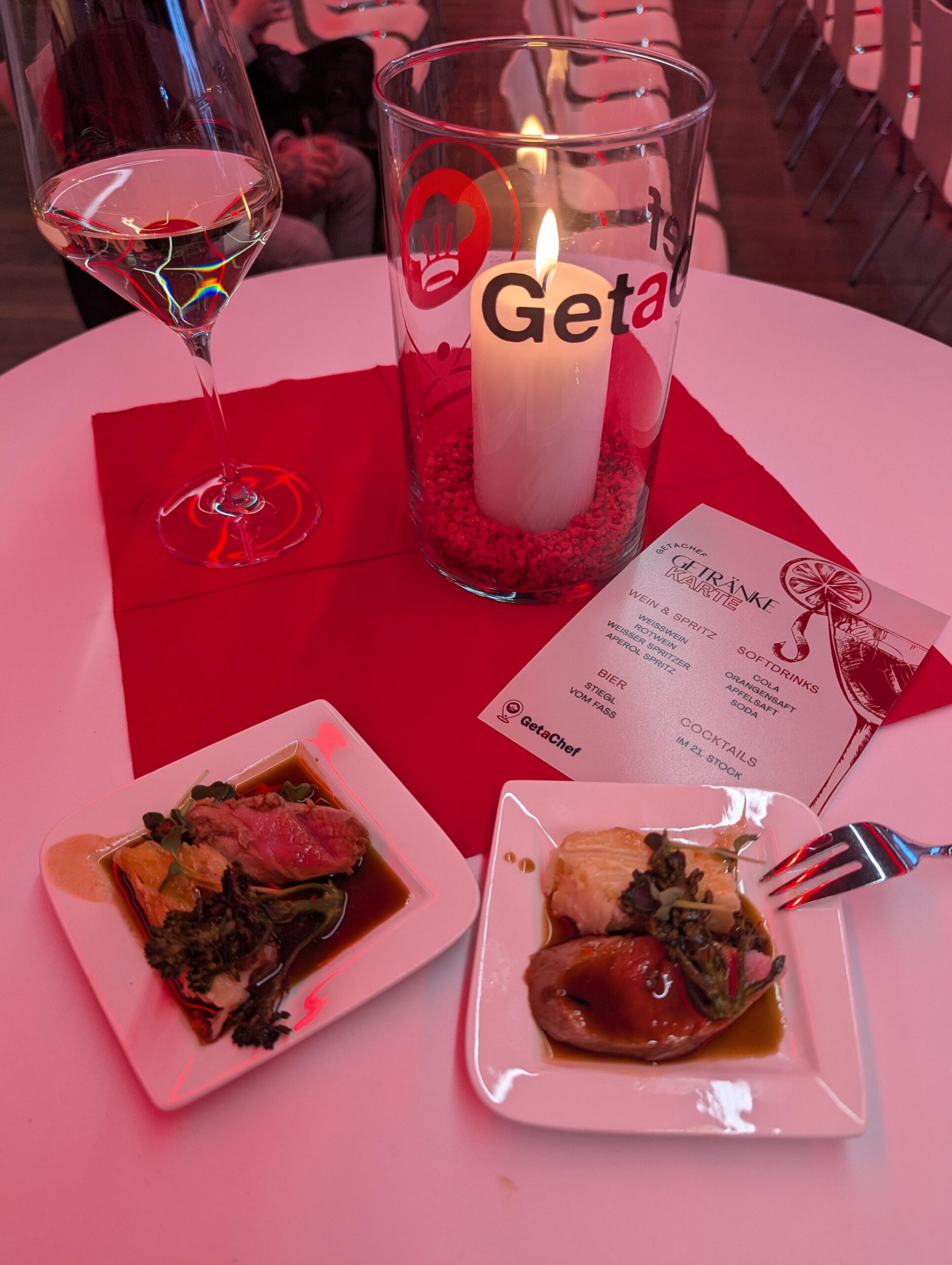 Weißweinglas, brennende Kerze im GetaChef-Glas, Getränkekarte und zwei kleine Teller mit Fingerfood auf der GetaChef Launch Party in Wien – entspannte Networking-Atmosphäre für App-Gründer.