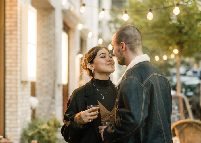 Paar steht nah beieinander bei einem entspannten Abend-Date mit Lichterkette im Hintergrund – echtes, authentisches Kennenlernen