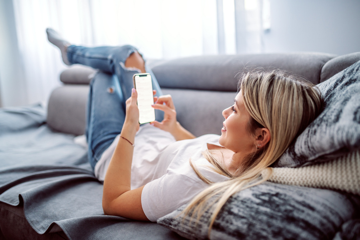Frau auf dem Sofa schaut aufs Smartphone – Match aufgelöst und Funkstille beim Online-Dating (Ghosting).