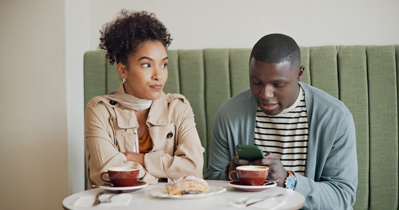 Zwei Personen im Café, eine wirkt genervt während der andere aufs Handy schaut – Situationship und fehlende Klarheit beim Dating