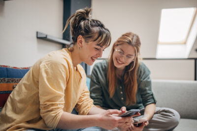 Zwei Freundinnen schauen gemeinsam aufs Smartphone als Symbol für Friendfluence, soziales Dating und gemeinsame Einschätzung von Matches