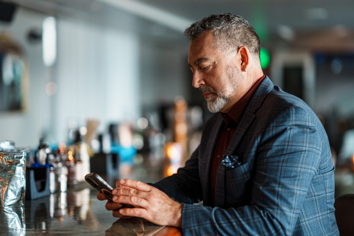 Mann in gepflegter Kleidung schaut in einer Bar auf sein Smartphone als Symbol für Parship, ernsthafte Partnersuche und anspruchsvolles Online-Dating