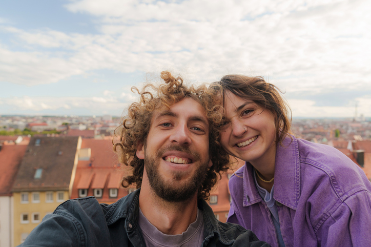 Lachendes Paar macht Selfie auf Dachterrasse mit Stadtblick – Symbol für erfolgreiches Online Dating und echte Verbindungen.