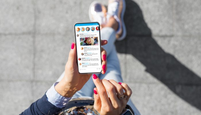 Frau nutzt Smartphone für soziale Medien, Symbolbild für den Dating-Trend Benching Eine Frau, die auf einem Bürgersteig sitzt und auf ihrem Smartphone eine Dating-App benutzt und benching befürchtet.